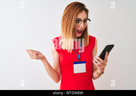 Redhead imprenditrice indossando id card utilizzando lo smartphone isolato su sfondo bianco urlando orgoglioso e celebrando la vittoria e il successo molto eccitato Foto Stock