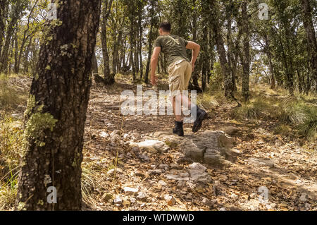 Attivo e sano giovane uomo escursionismo una collina nella foresta di alberi e foglie Foto Stock