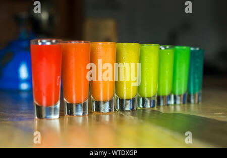 Un gruppo di bicchierini con un arcobaleno di bevande colorate al tavolo di un rustico bar in Messico Foto Stock