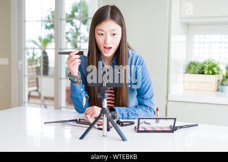 Bella asiatica influencer donna la registrazione compongono tutorial utilizzando la fotocamera dello smartphone paura in stato di shock con una sorpresa faccia paura ed eccitato con la paura Foto Stock