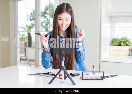 Bella asiatica influencer donna la registrazione compongono tutorial utilizzando la fotocamera dello smartphone urlando orgoglioso e celebrando la vittoria e il successo molto eccitato, Foto Stock