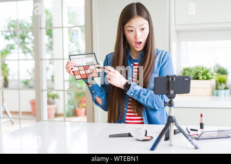 Bella asiatica influencer donna la registrazione compongono tutorial utilizzando la fotocamera dello smartphone paura in stato di shock con una sorpresa faccia paura ed eccitato con la paura Foto Stock