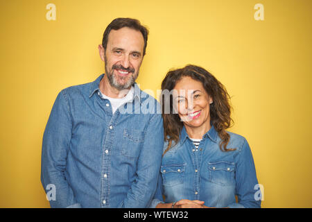 Bella la mezza età giovane insieme in piedi isolato su sfondo giallo con mani e dita incrociate sorridendo rilassato e allegro. Su Foto Stock