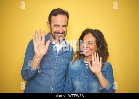 Bella la mezza età giovane insieme in piedi isolato su sfondo giallo rinuncia a dire ciao felice e sorridente, gentile gesto di benvenuto Foto Stock