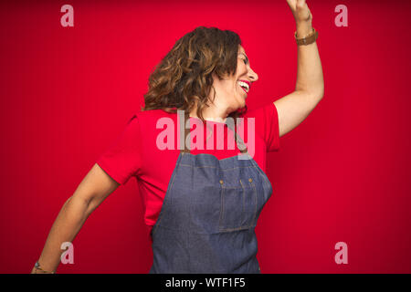 La mezza età senior donna che indossa il grembiule uniforme su rosso sfondo isolato Dancing felice e allegro e sorridente spostamento casuale e di ascolto fiducioso t Foto Stock