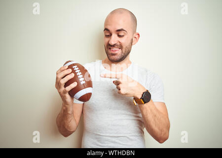 Giovane Azienda rugby football americano palla su sfondo isolato molto felice puntando con mani e dita Foto Stock