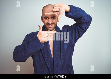 Giovane uomo indossare accappatoio blu, stile di vita rilassato su sfondo isolato sorridente rendendo il telaio con le mani e le dita con la faccia felice. La creatività di un Foto Stock