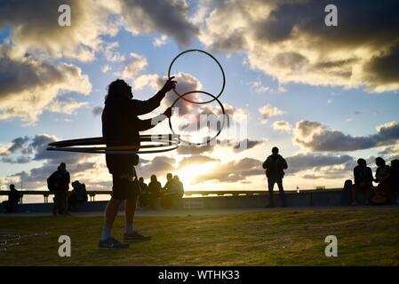 L'uomo la pratica di anelli di filatura hoops nel parco, con bohemien, hippie folla rilassante durante il tramonto, Ocean Beach (OB) a San Diego, California, Stati Uniti d'America Foto Stock