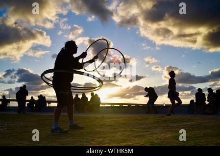 L'uomo la pratica di anelli di filatura hoops nel parco, con bohemien, hippie folla rilassante durante il tramonto, Ocean Beach (OB) a San Diego, California, Stati Uniti d'America Foto Stock