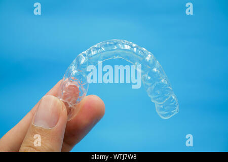 Mano che tiene in plastica trasparente con denti di ritegno che isolato sul cielo azzurro sfondo. Si tratta di una apparecchiatura di ortodontista dare al paziente di ortodonzia sur Foto Stock