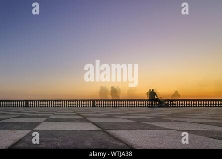 Ombre e sagome delle persone che camminano sulla terrazza che si affaccia sul mare al tramonto Foto Stock