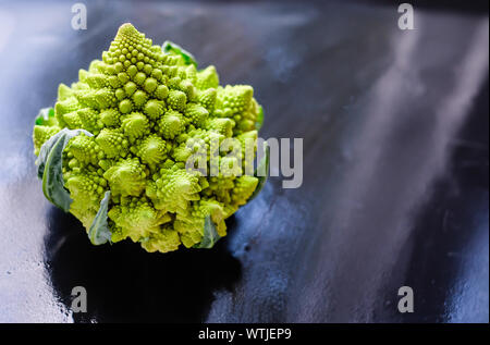 Sorprendente fresco broccoli Romanesco verde o cavolfiore romano su fondo umido scuro. La sua forma è un'approssimazione naturale di un frattale. Vista ravvicinata.
