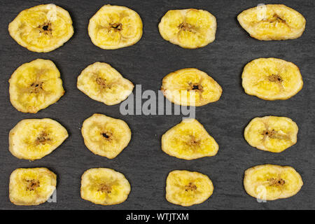 Sacco di fette di dolce secco giallo banana flatlay sulla pietra grigia Foto Stock