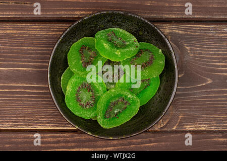 Sacco di fette di dolci verdi canditi di kiwi in scuro vaso di ceramica flatlay su legno marrone Foto Stock