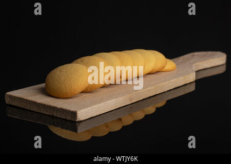 Gruppo di otto tutto il dolce e dorato biscotto di spugna sul piccolo tagliere di legno isolata sul vetro nero Foto Stock