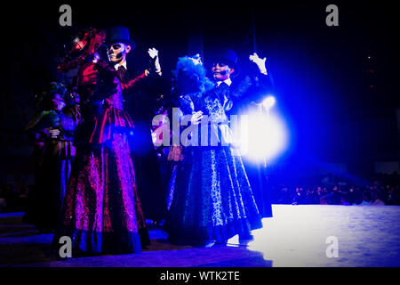 Merida, Messico - 27 Ottobre 2018: Balli Catrina coppie con cranio compongono per dias de los Muertos con abiti tradizionali con retroilluminazione a Remate de Paseo Montejo al Festival de las animas Foto Stock