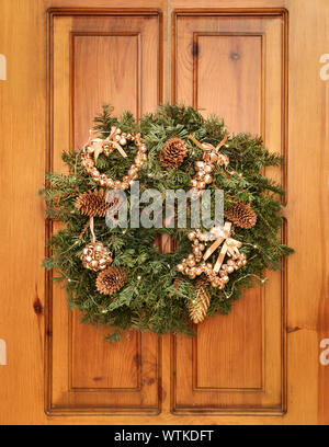Natale e Anno Nuovo ghirlanda di rami di abete con coni sulla porta di casa. La corona è decorata con vintage toys dalla polvere rosa le campane in Foto Stock