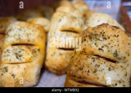 Primo piano di dolci salati appena sfornati conditi con erbe e formaggio disposti in mostra in una panetteria Foto Stock
