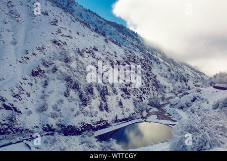 Piccolo lago pictersque nelle montagne innevate parzialmente coperto da nuvole Foto Stock