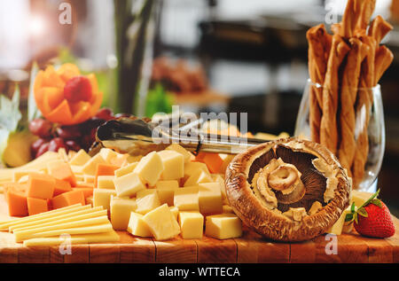 Rustico mix di tagli di formaggio, funghi e frutti su un tagliere di legno, durante il brunch a buffet. Gustoso assortimento di formaggi freschi selezione, vari tipi o Foto Stock