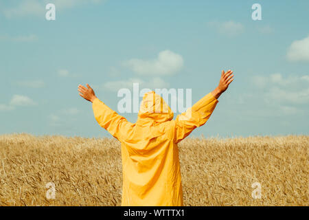 Felice giovane uomo che indossa un impermeabile giallo in piedi in un campo di grano Foto Stock