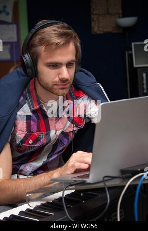 Focalizzato giovane uomo in cuffia la composizione su un laptop, pianoforte, tastiera Foto Stock