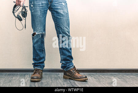 Moda giovane uomo in jeans e scarpe con le cuffie sul pavimento in legno Foto Stock