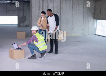 Ingegner architetto utilizzando computer portatile mentre mostra house design piani per una giovane coppia multietnica al sito in costruzione Foto Stock