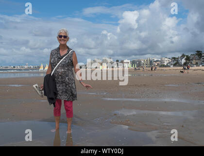 Una donna anziana passeggiate sulla spiaggia sorridente Foto Stock