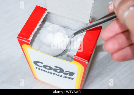 Carbonato di sodio in polvere in un cucchiaio. Soda da una scatola di cartone. La guarnizione sul tavolo in cucina Foto Stock