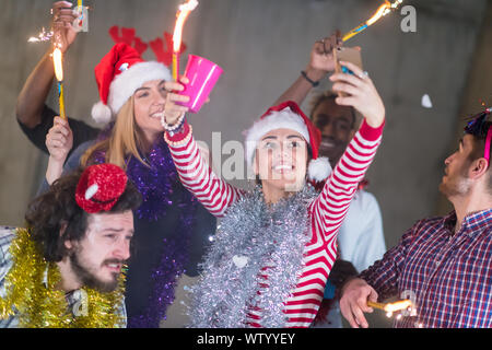 Gruppo multietnico di giovani felici informali di lavoro persone tenendo selfie foto mentre ballando con botti e divertirsi durante la festa di capodanno in fro Foto Stock