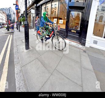 Londra, Inghilterra, Regno Unito. Donna in bicicletta sul marciapiede, su un noleggio di Santander-bike Foto Stock