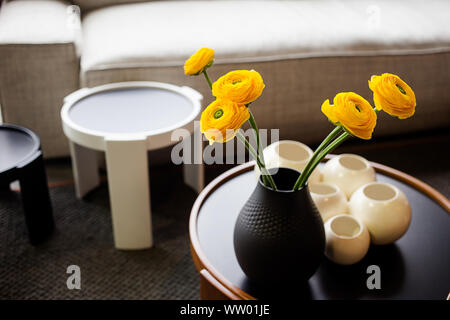 Bouquet di roselline (Ranunculus asiaticus) in un vaso nero. Fiori di colore giallo all'interno. Foto Stock