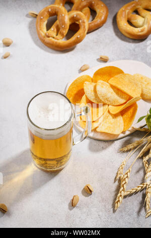 Un boccale di birra chiara con il tedesco pretzel e chip su sfondo grigio chiaro. Copia dello spazio. Foto Stock