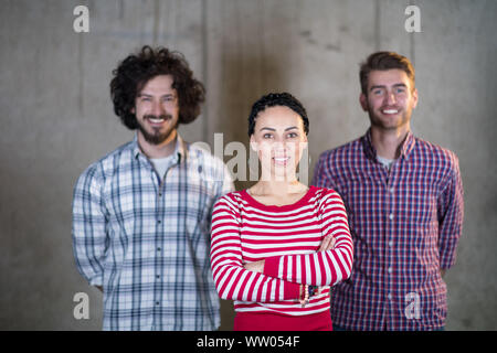 portrait of young successful smiling casual business team standing in front of a concrete wall at new startup office Foto Stock