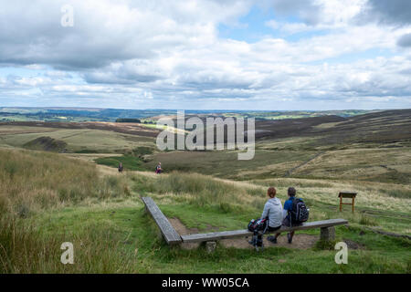 Due escursionisti guardare indietro sulla vista dal recinto Pennine Way al Top Withens su Stanbury Moor verso Haworth nel West Yorkshire, Inghilterra. Foto Stock