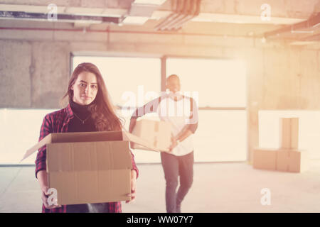 Felice giovani casual multietnica team aziende che trasportano le scatole di cartone con la luce del sole attraverso le finestre durante il passaggio al nuovo avvio incompiuto off Foto Stock