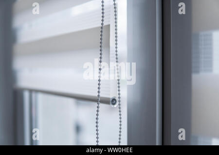 Dettagli di tessuto bianco tende a rullo sulla parte in plastica bianca finestra nel soggiorno. Close up sul rotolo tende indoor. Foto Stock