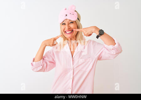 Medioevo donna che indossa la maschera del sonno e pigiama isolato su sfondo bianco sorride mostrando allegro e indicando con le dita dei denti e della bocca. Dent Foto Stock