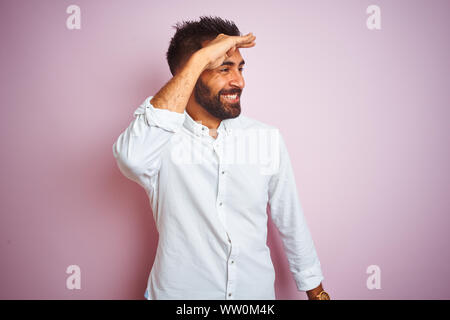 Giovane imprenditore indiano indossando maglietta elegante in piedi isolato su sfondo rosa molto felice e sorridente guardando lontano con la mano sopra la testa. Il mare Foto Stock