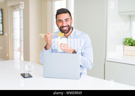 Uomo d'affari di mangiare cibo asiatico dalla consegna mentre si lavora con il computer portatile in ufficio Foto Stock