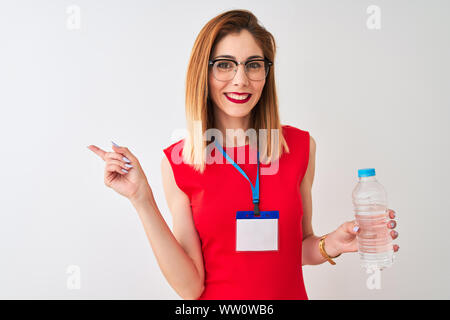 Redhead imprenditrice indossando id card acqua potabile isolato su sfondo bianco molto felice rivolto con la mano e le dita per lato Foto Stock