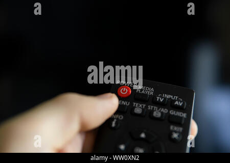 Chiudere in su su una mano d'uomo con il telecomando desidera accendere il TV e preme il pulsante sul telecomando. Telecomando in mano closeup. Foto Stock