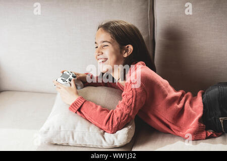 Niña jugando en casa con la videoconsola tumbada en el divani Foto Stock