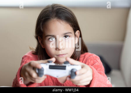 Niña jugando en casa con la videoconsola tumbada en el divani Foto Stock