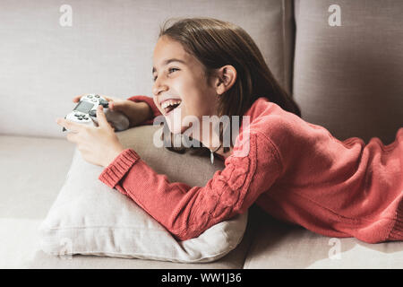 Niña jugando en casa con la videoconsola tumbada en el divani Foto Stock