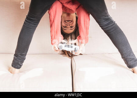 Niña jugando en casa con la videoconsola sentada en el divani Foto Stock