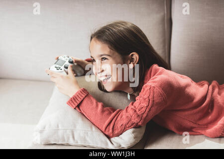 Niña jugando en casa con la videoconsola tumbada en el divani Foto Stock