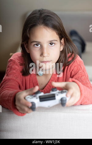 Niña jugando en casa con la videoconsola tumbada en el divani Foto Stock