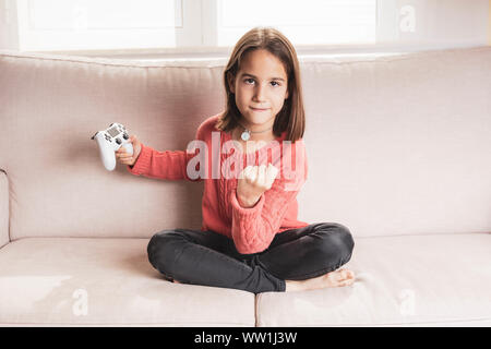 Niña jugando en casa con la videoconsola sentada en el divani Foto Stock